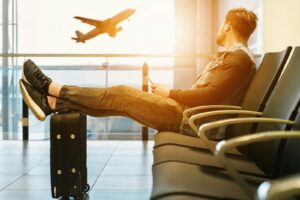 Traveller resting beside a suitcase while watching an aircraft through an airport window